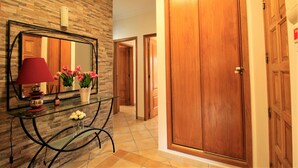 Un pasillo con una puerta de madera, un espejo y una mesa de vidrio con flores.