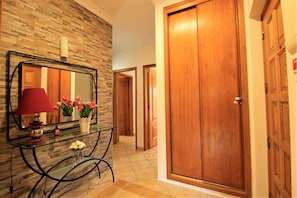 Un pasillo con una puerta de madera, un espejo y una mesa de vidrio con flores.