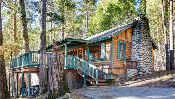 Een chalet met een stenen schoorsteen, een houten terras en een trap naar een veranda.
