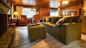 Een gezellig interieur van een blokhut met houten plafond, een groene bank, een klein tafeltje en een plafondventilator.