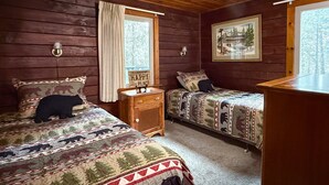 Een kamer in chaletstijl met twee bedden, houten wanden, een raam met gordijnen, een nachtkastje en een schilderij aan de muur.