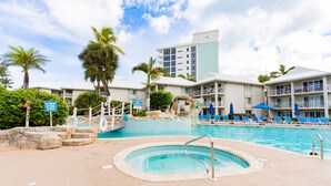 Un espace piscine d’hôtel avec un jacuzzi, des chaises longues et des palmiers.