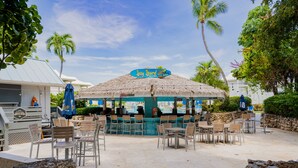 Un bar situé en bord de mer, doté d’un toit de chaume, de tables à l’extérieur et de palmiers.