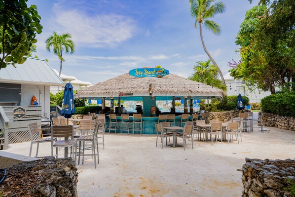 A beachside bar with a thatched roof, outdoor seating, and palm trees.