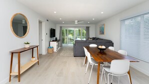 Un salon moderne avec une table à manger en bois, des chaises blanches, un canapé gris et un grand miroir.