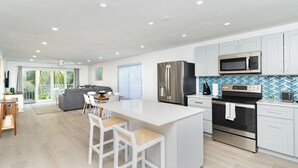 Une cuisine moderne avec des meubles blancs, un îlot central doté de tabourets, des appareils en acier inoxydable et un dosseret de carrelage disposé en motif chevrons.