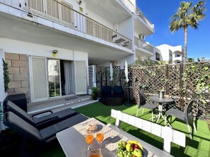 Ein zweistöckiges Gebäude mit Balkonen, einer Terrasse mit Gartenmöbeln und einem Tisch mit Früchten und Getränken.