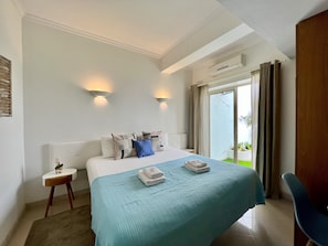 Ein Hotelzimmer mit einem großen Bett, zwei Wandleuchten, einem kleinen Nachttisch und Blick ins Freie durch eine Schiebetür.