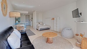 A modern living room with a black leather sofa, a round wooden coffee table, a bed with striped bedding, a white bean bag, and a television mounted on the wall. - Quinta DO Lago Victory Village With Pool (Loulé)