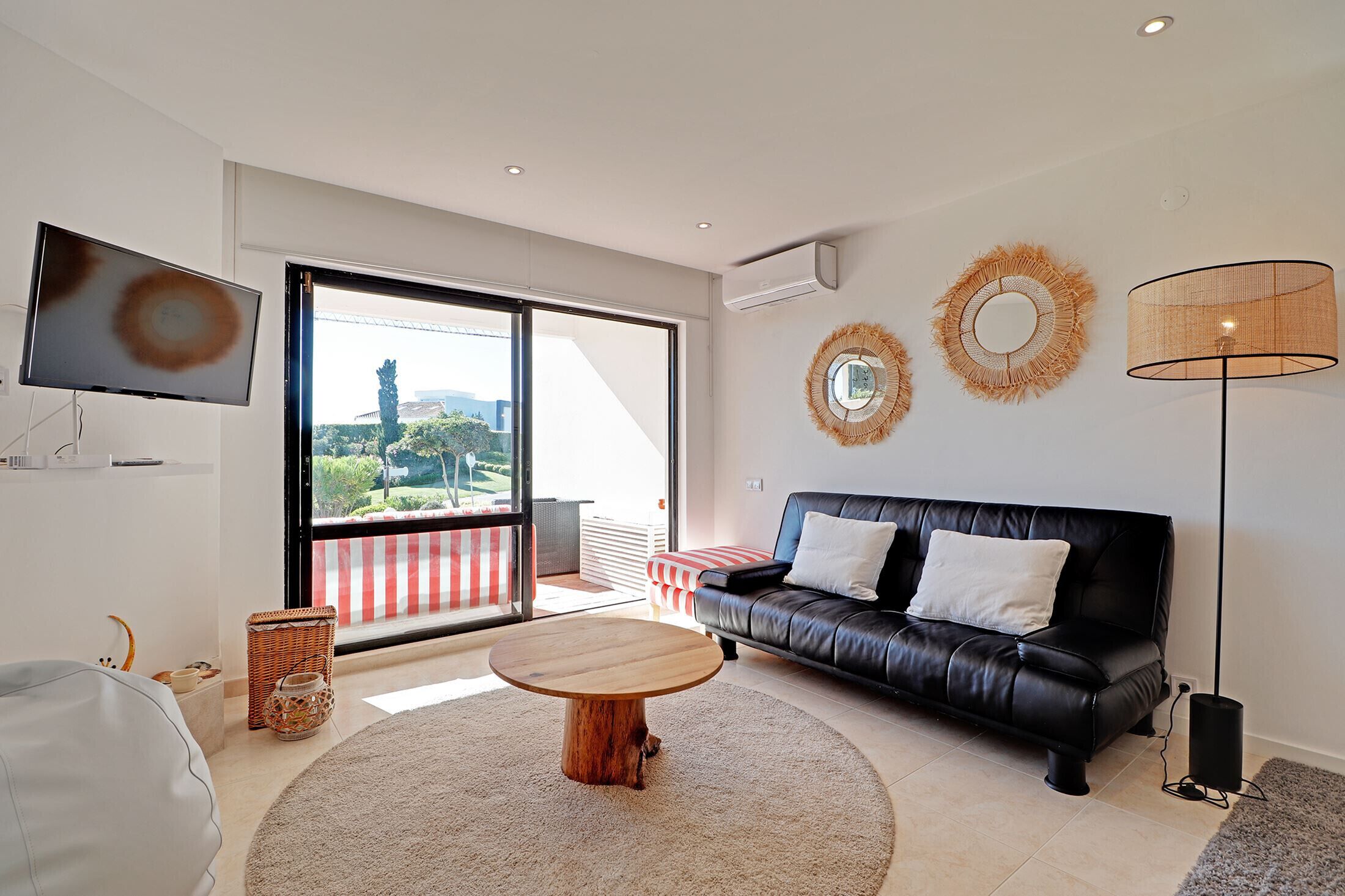 A modern living room with a black leather sofa, a round wooden coffee table, and a large sliding glass door leading to an outdoor area.