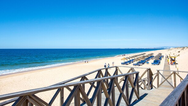 A wooden boardwalk leading to a beach with rows of blue lounge chairs and umbrellas. - Quinta DO Lago Victory Village With Pool (Loulé)