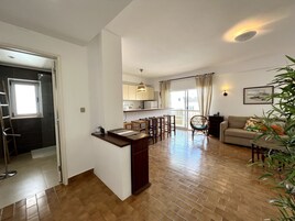 Amplia sala de estar con piso de madera, una mesa de comedor con sillas, un sofá y una pequeña cocina con ventana.