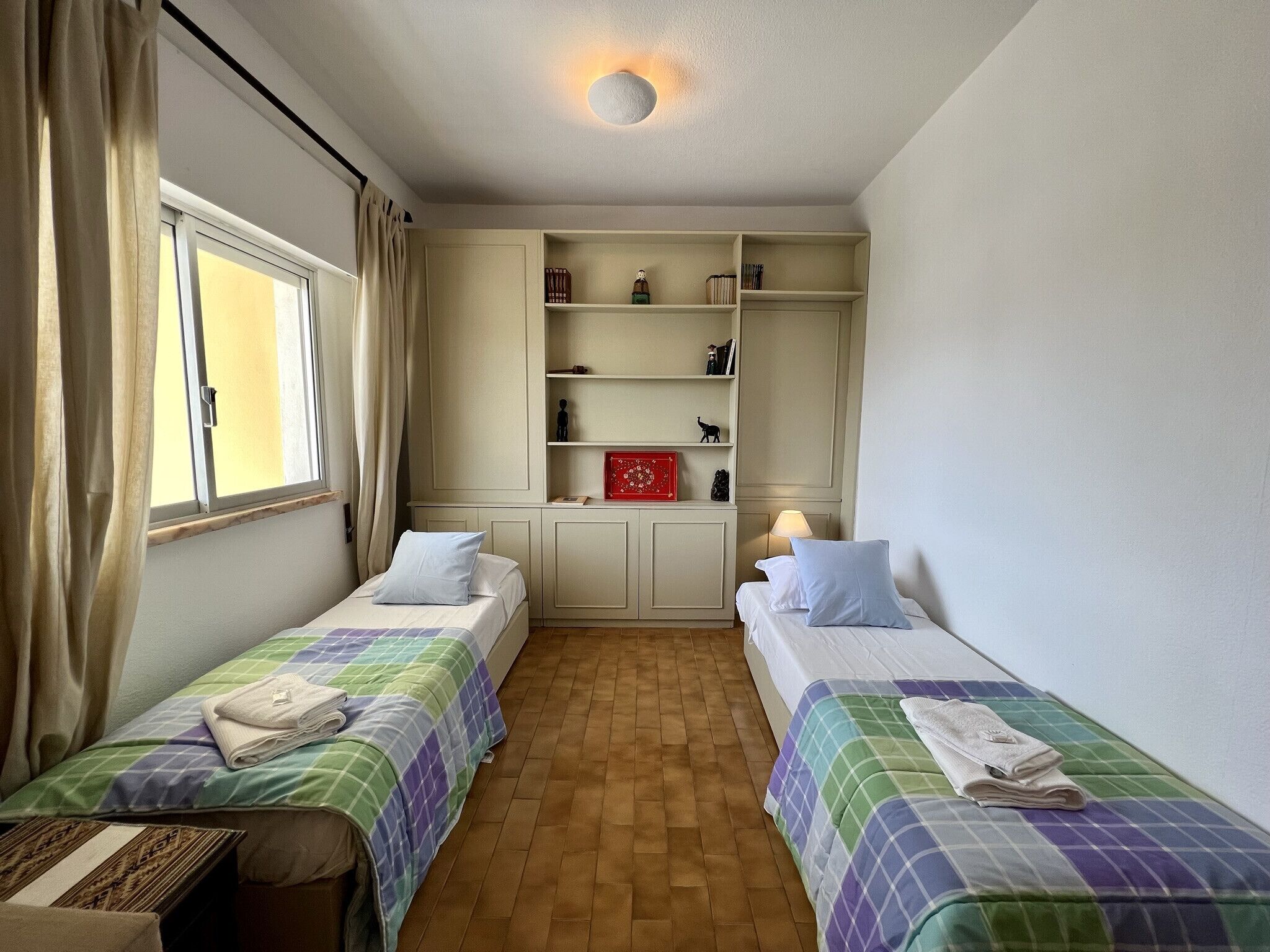A room with two single beds, a wardrobe, and a window with curtains.