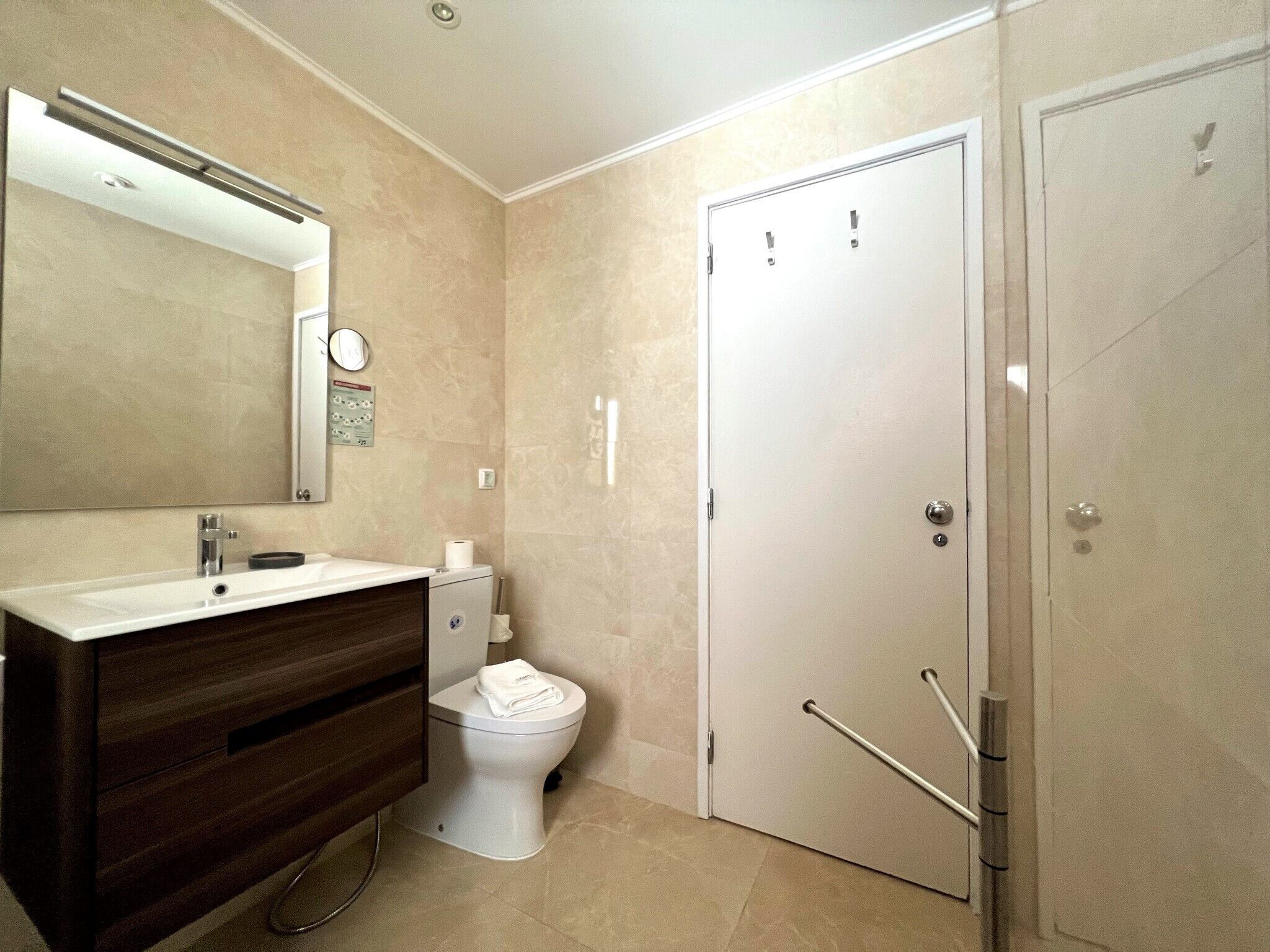 A modern bathroom with a white vanity, a toilet, and a door with a handle and a towel rack.