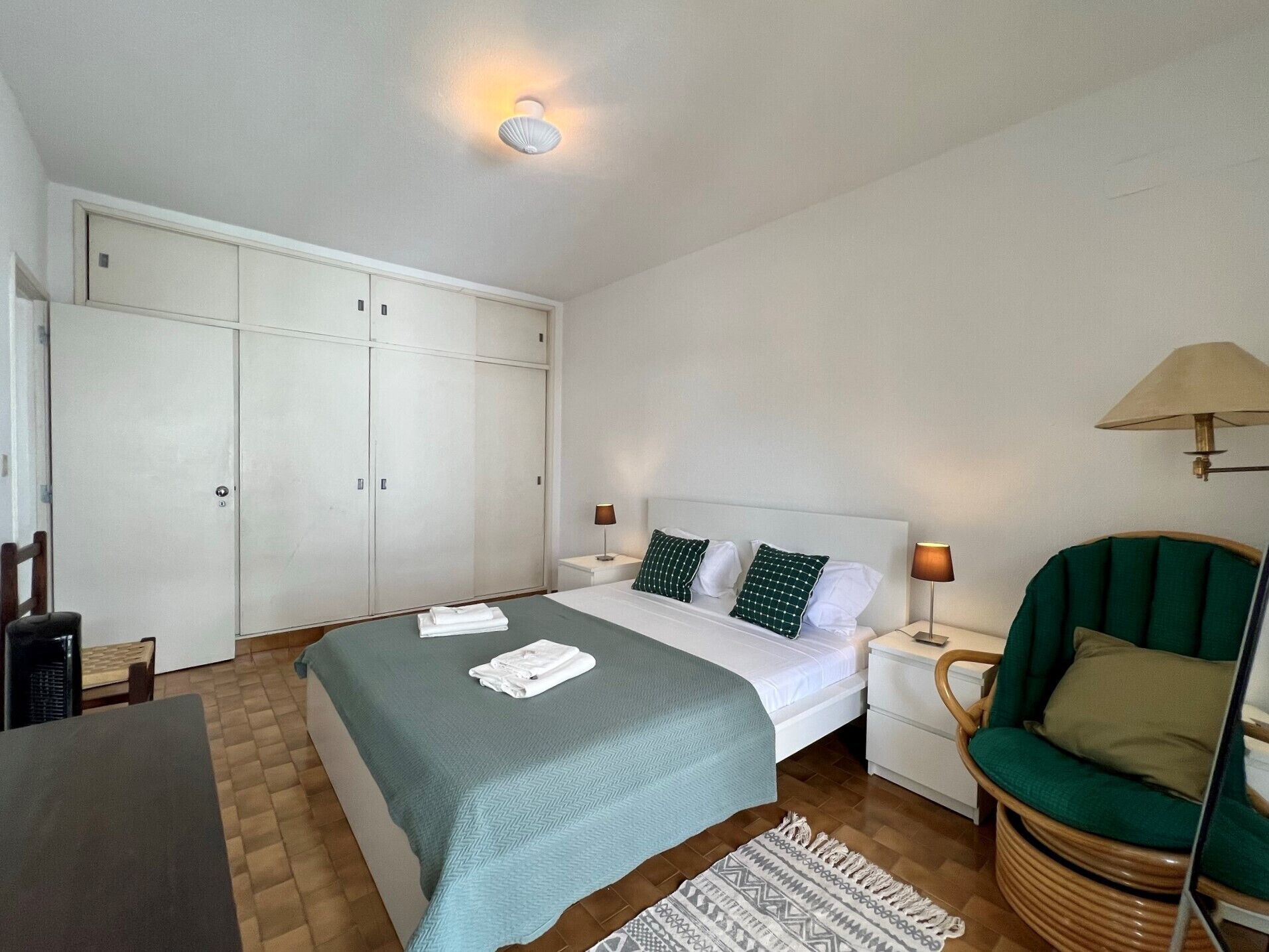 Une chambre à coucher comprenant un lit, des tables de chevet, une chaise, une armoire et une lampe.