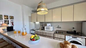 Een moderne keuken met witte kasten, een magnetron, een spoelbak en een schaal fruit op het aanrecht.
