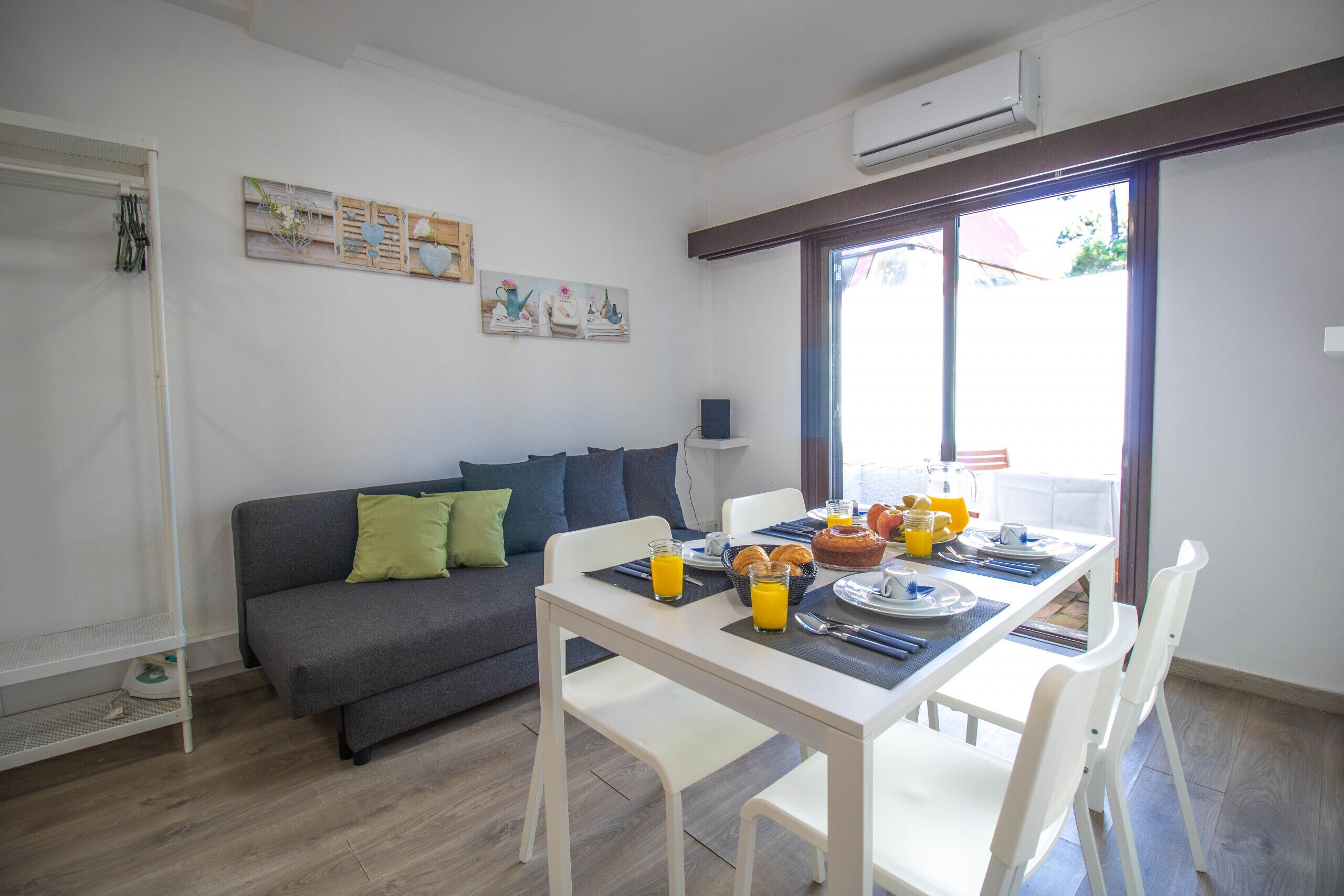 A dining area with a table set for breakfast, a gray sofa with pillows, and artwork on the wall.