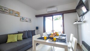 A dining area with a table set for breakfast, a sofa with cushions, a TV mounted on the wall, and a window with a view. - Vilamoura Golf Studio With Pool (Loulé)