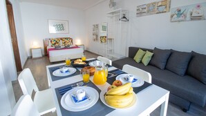A dining area with a table set for breakfast, a sofa, and a white cabinet with a fan. - Vilamoura Golf Studio With Pool (Loulé)