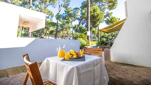 A table set outdoors with a white tablecloth, a wooden chair, a pitcher of orange juice, a plate of fruit, and a bottle of water. - Vilamoura Golf Studio With Pool (Loulé)