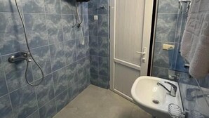 A bathroom with blue tiles, a white sink, a handheld showerhead, and a toilet. - Hotel Laguna (Ureki)