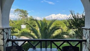 An outdoor seating area with a table and two chairs, framed by a stone archway overlooking a lush landscape with trees and a clear sky. - Hotel Laguna (Ureki)