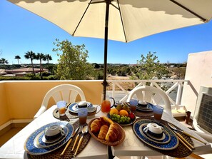 A balcony table set with breakfast items, including croissants, fruit, and tea, under a large umbrella with a scenic view. - Albufeira Valley 1 With Pool by Homing (Albufeira)
