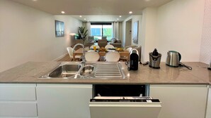 A modern kitchen with a dishwasher, a sink, and a dining area with chairs and a table. - Faro Design 6 by Homing (Faro)