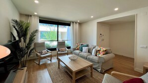 A modern living room with a sofa, two armchairs, a coffee table, and a TV. There is a large window with curtains, a potted plant, and a door leading to another room. - Faro Design 6 by Homing (Faro)