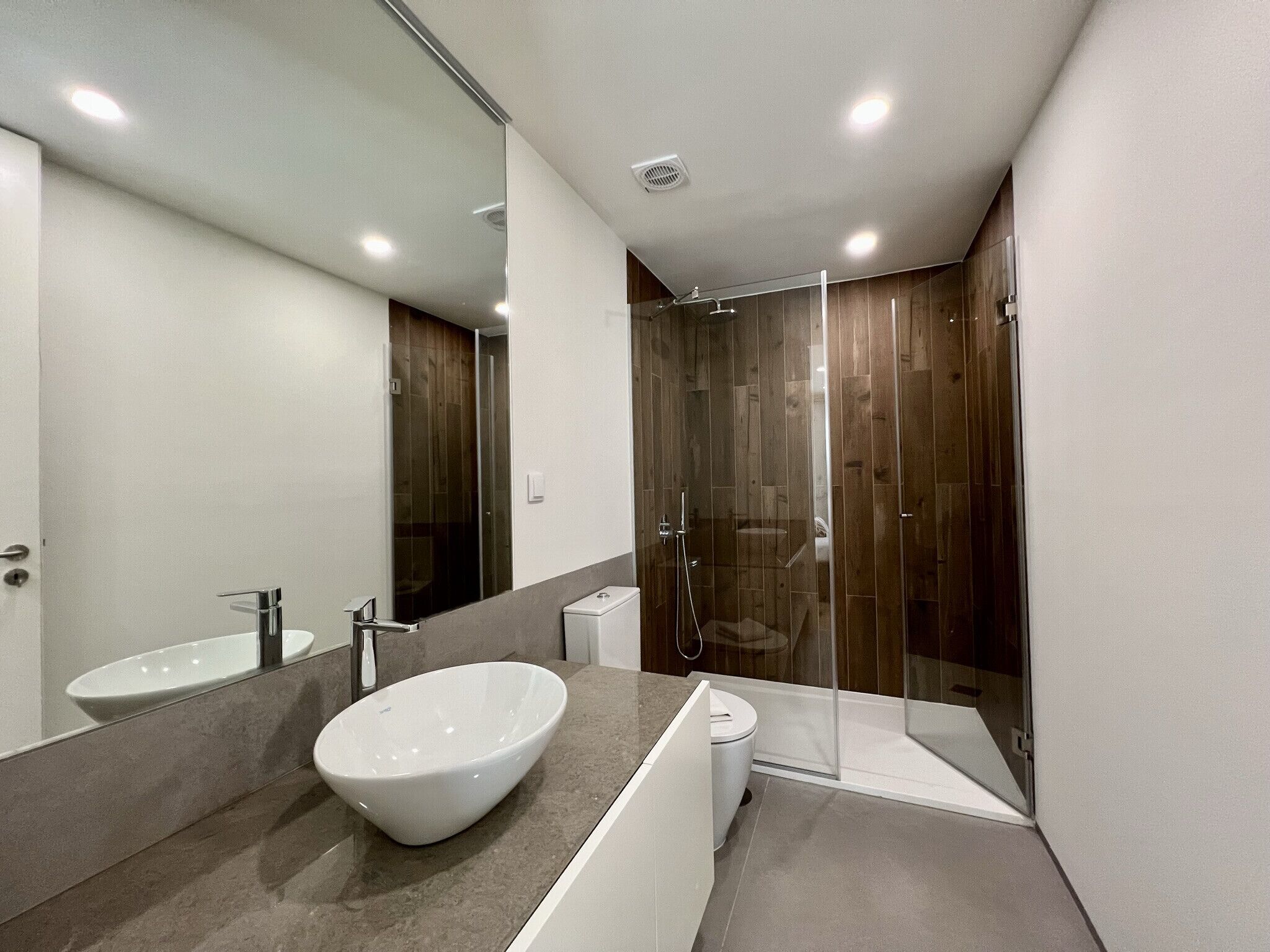 A modern bathroom with a large white basin, a glass-enclosed shower, and a toilet.