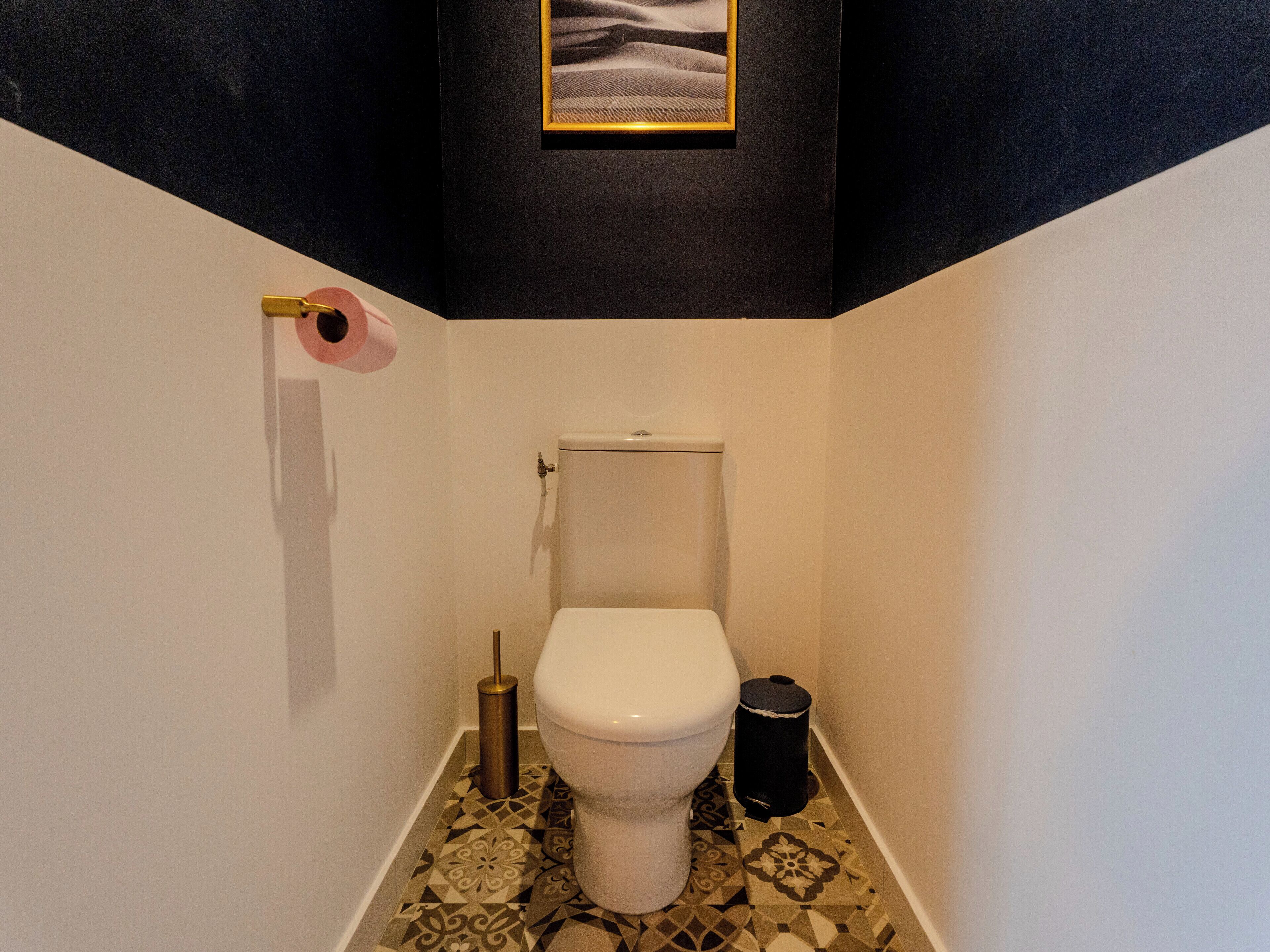 A small, narrow bathroom with a toilet, a trash bin, and a toilet paper holder.