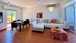Un salón moderno con sofá, mesa de comedor, sillas y una mesita con una cesta tejida.