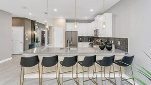 A modern kitchen with a central island, bar stools, pendant lighting, and a backsplash. - The Best Value by All Vacation (Kissimmee)