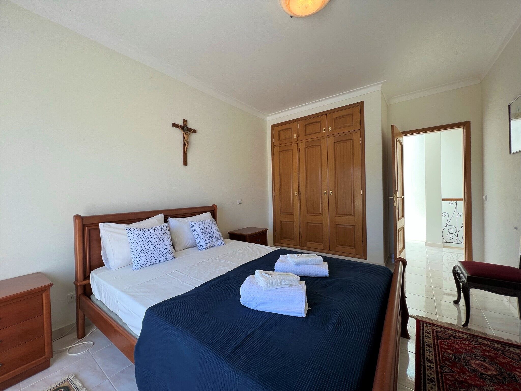A bedroom with a wooden bed, a cross on the wall, and a wardrobe.