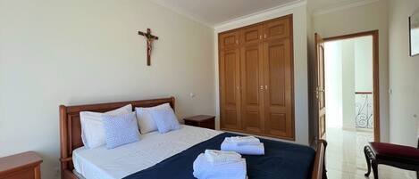 A bedroom with a wooden bed, a cross on the wall, and a wardrobe.