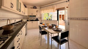 A kitchen with white cabinets, a dining table with chairs, and a window with curtains. - Lagos Typical House by Homing (Lagos)