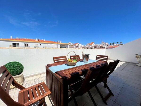 A rooftop terrace with a wooden table and chairs, a metal bucket, and a basket of fruit. - Lagos Typical House by Homing (Lagos)