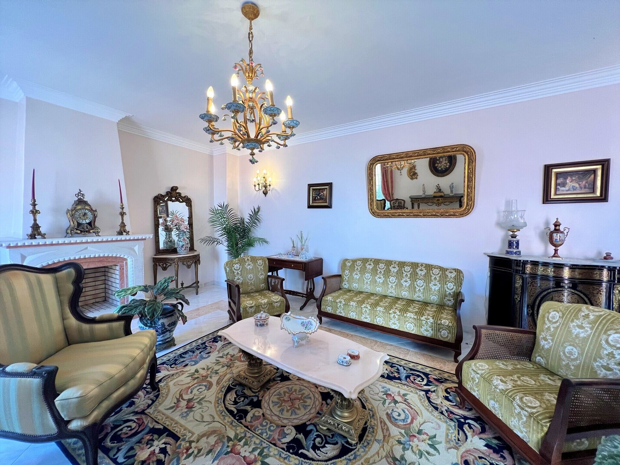A traditional living room with a fireplace, ornate chandelier, and classic furniture.