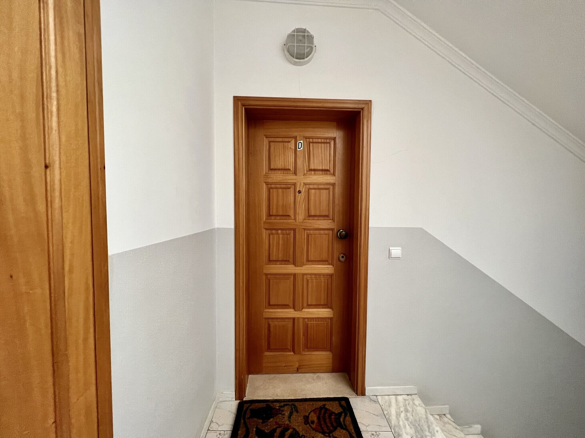A wooden door with a light switch on the wall above it.