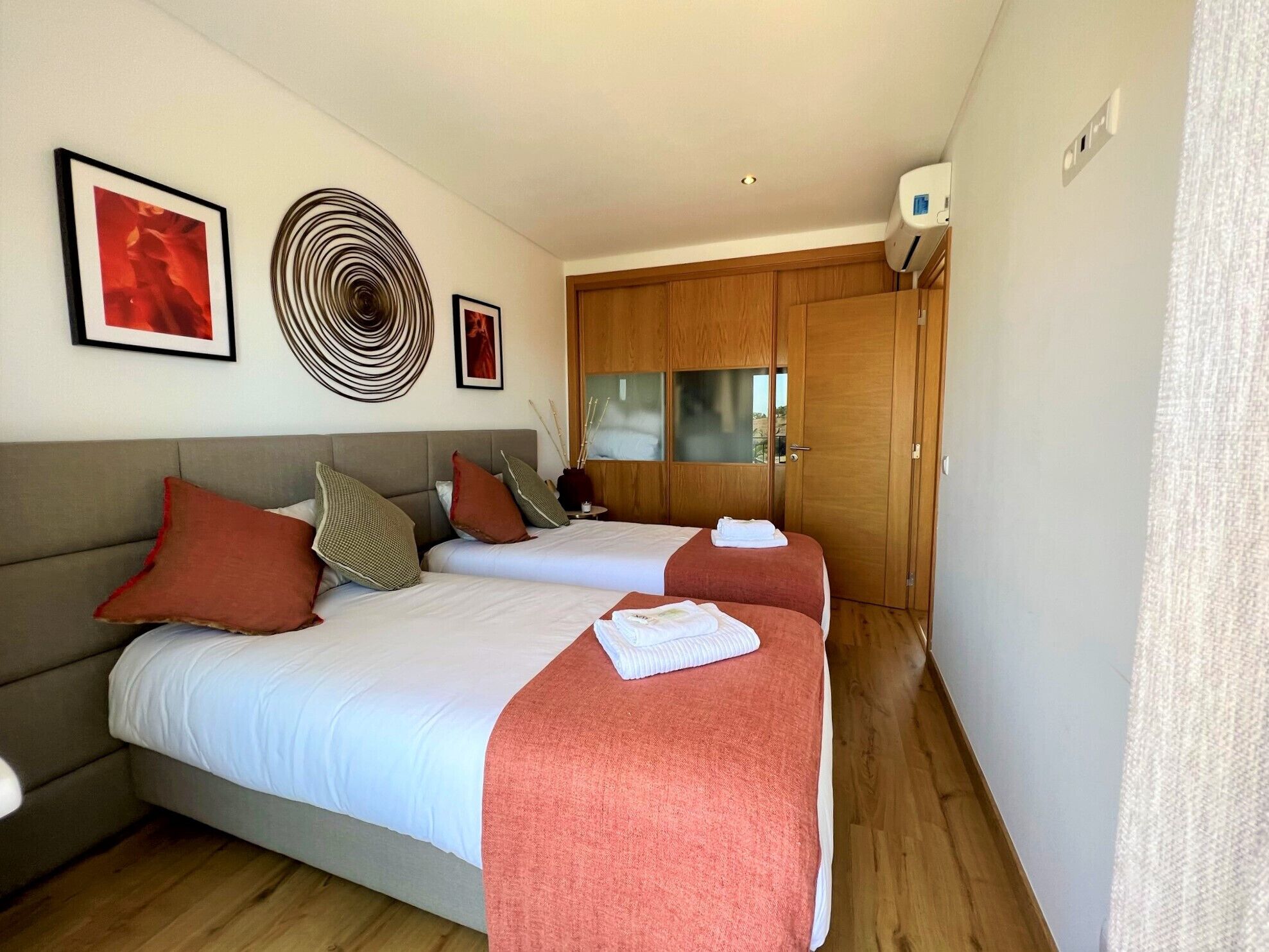 A hotel room with two beds, a sofa, and a wooden wardrobe.