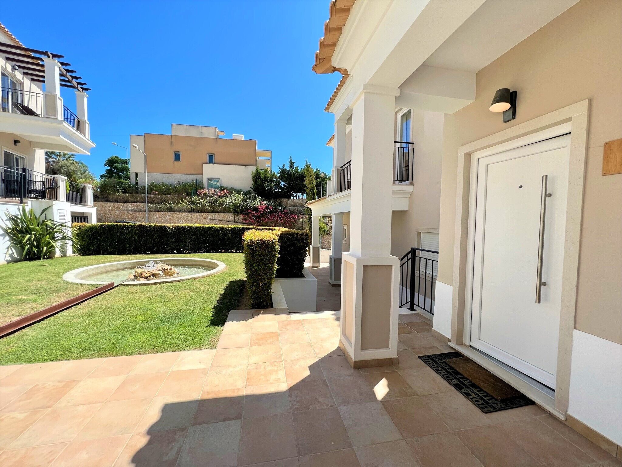 Un edificio residencial con un jardín bien cuidado, una pequeña fuente y un patio con baldosas.