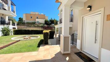 Un edificio residencial con un jardín bien cuidado, una pequeña fuente y un patio con baldosas.