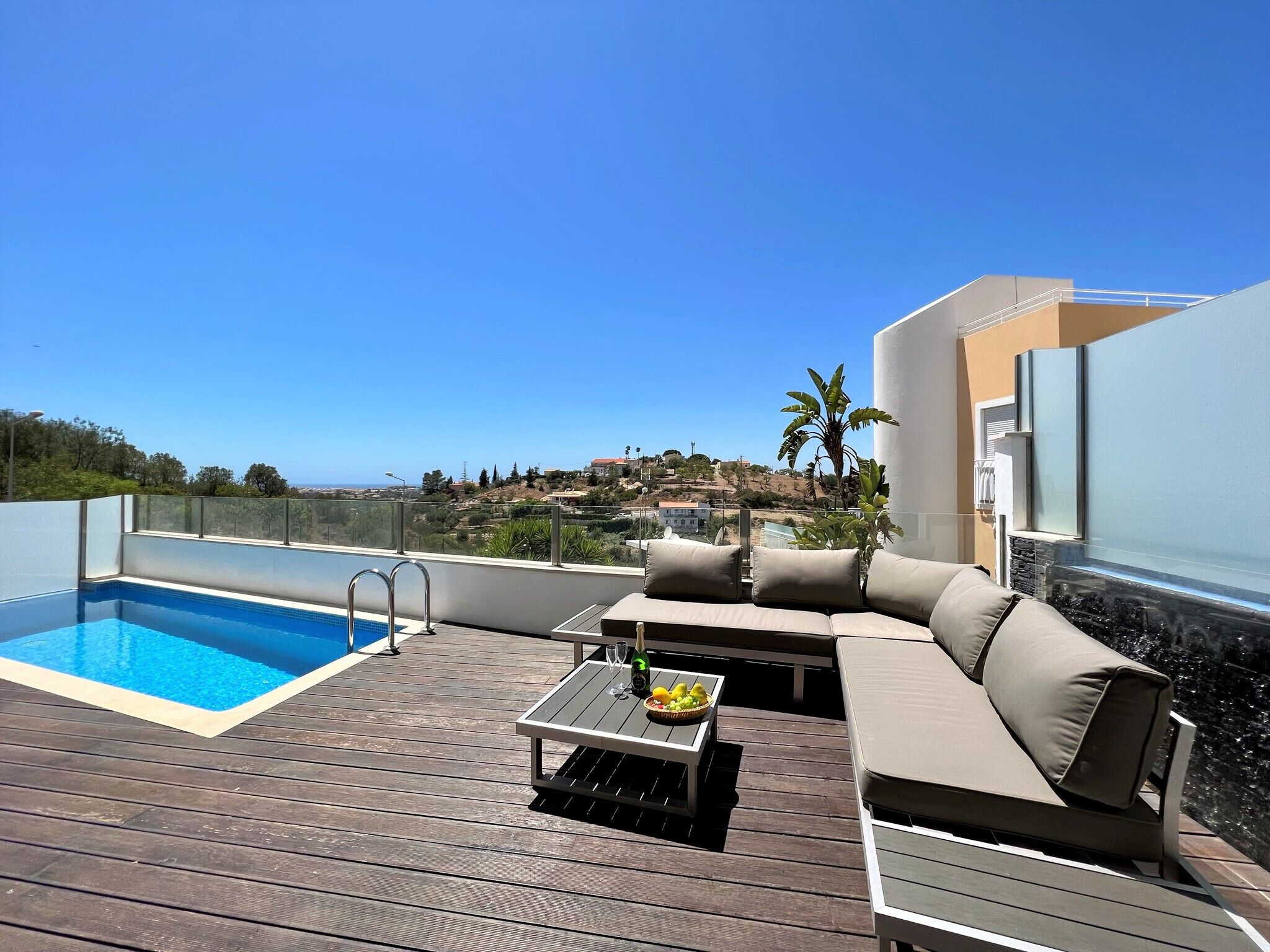 Zona de piscina al terrat amb piscina, zona d'estar amb coixins i taula amb una beguda i fruita.