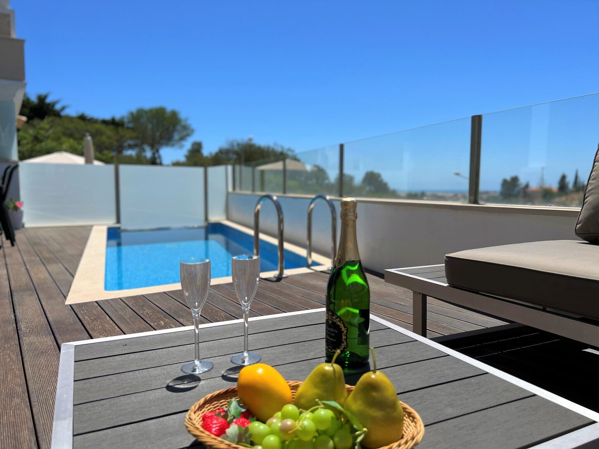 A poolside table with a bottle of champagne, two glasses, and a basket of fruit.