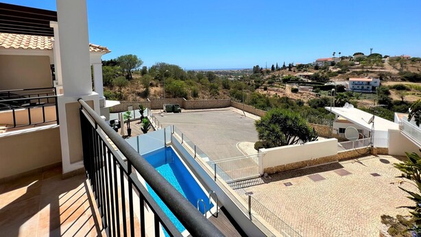 A balcony with a view of a swimming pool, a paved area, and surrounding buildings.