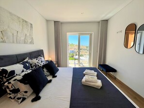 Ein modernes Hotelzimmer mit Bett, einer Couch, einem großen Fenster und Blick ins Freie.