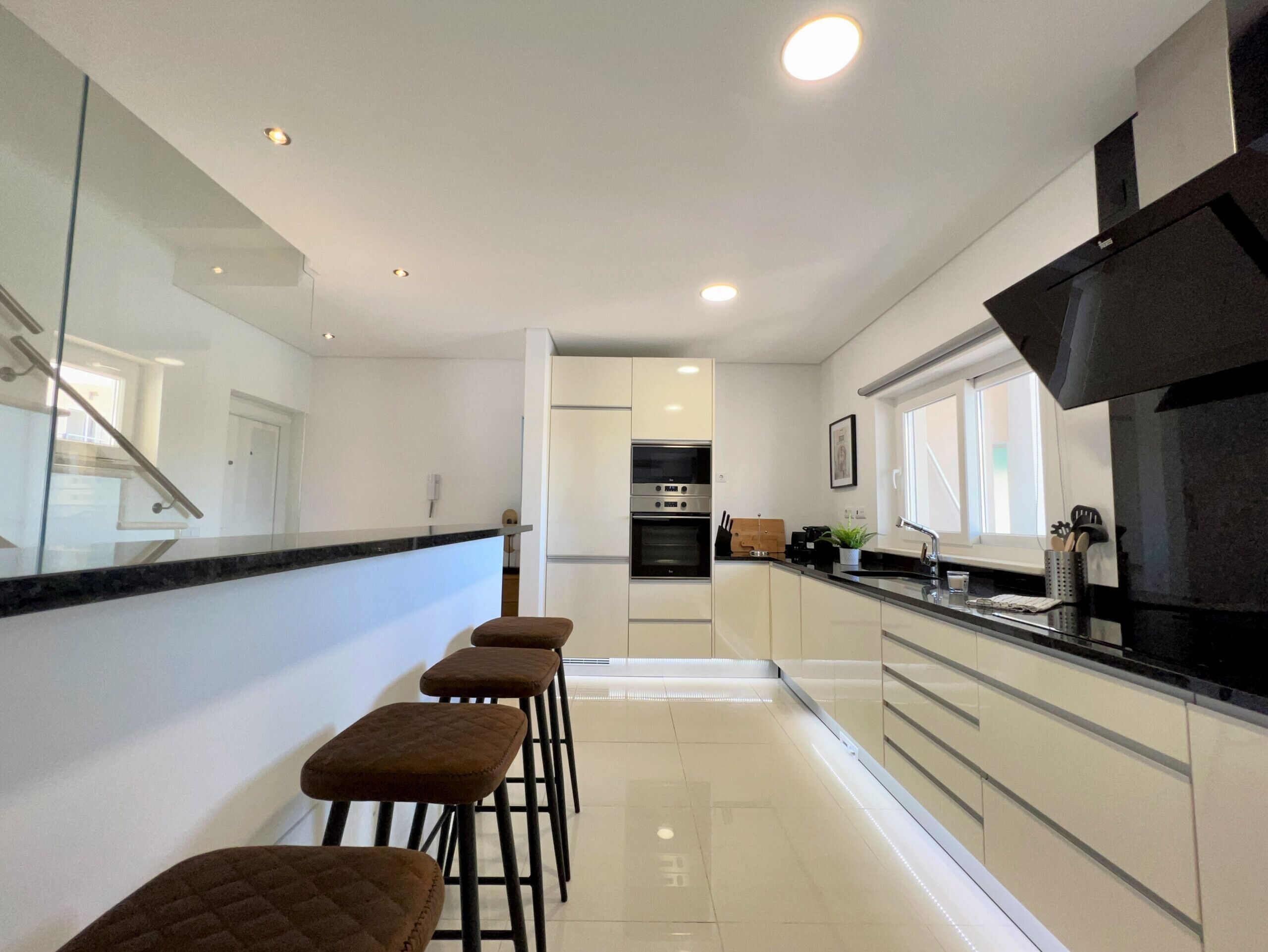 Una cocina moderna con una isla central, taburetes de bar y vista al área de estar.