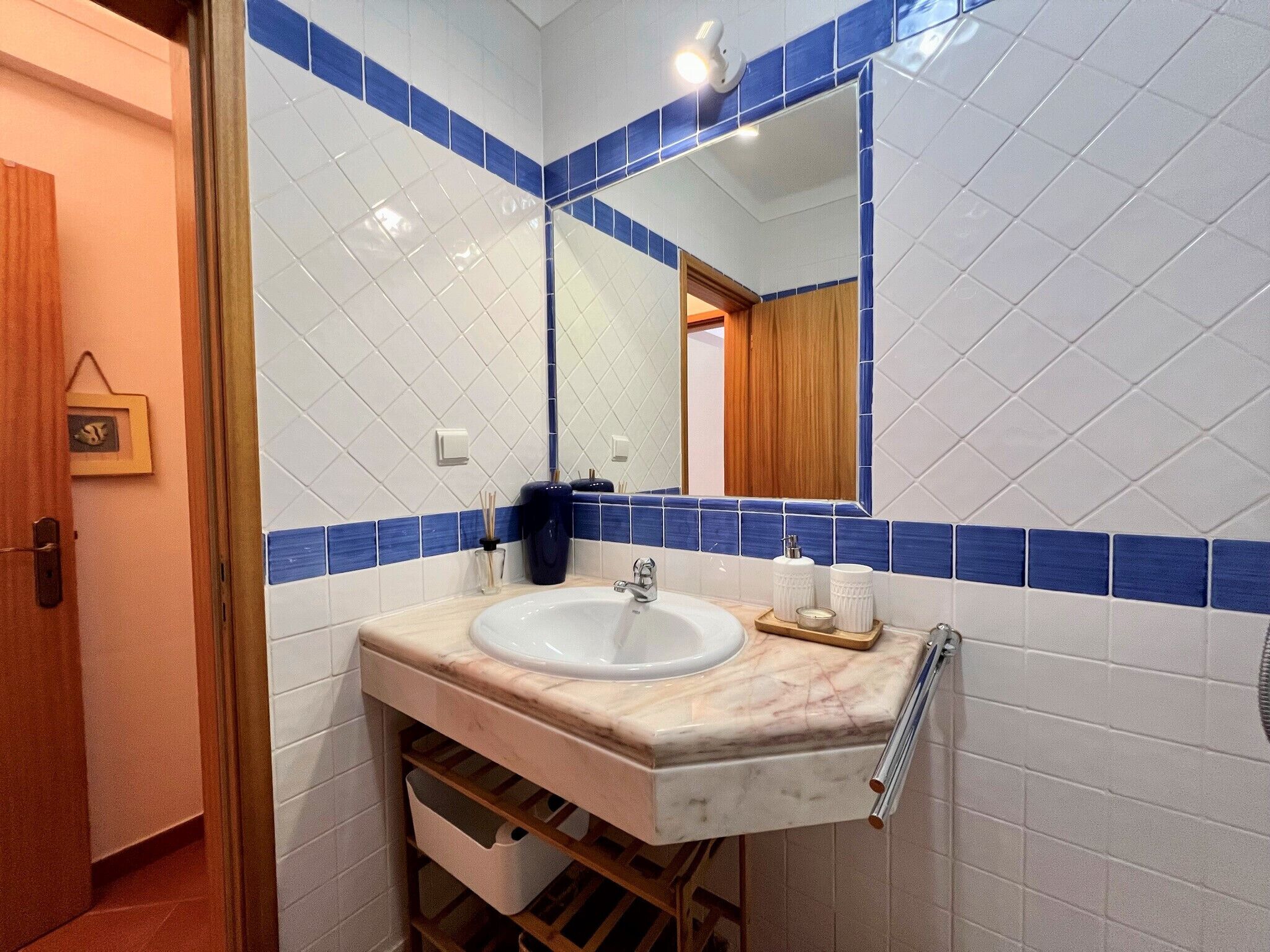 A bathroom with a white sink, blue-tiled walls, a wooden door, and a mirror.