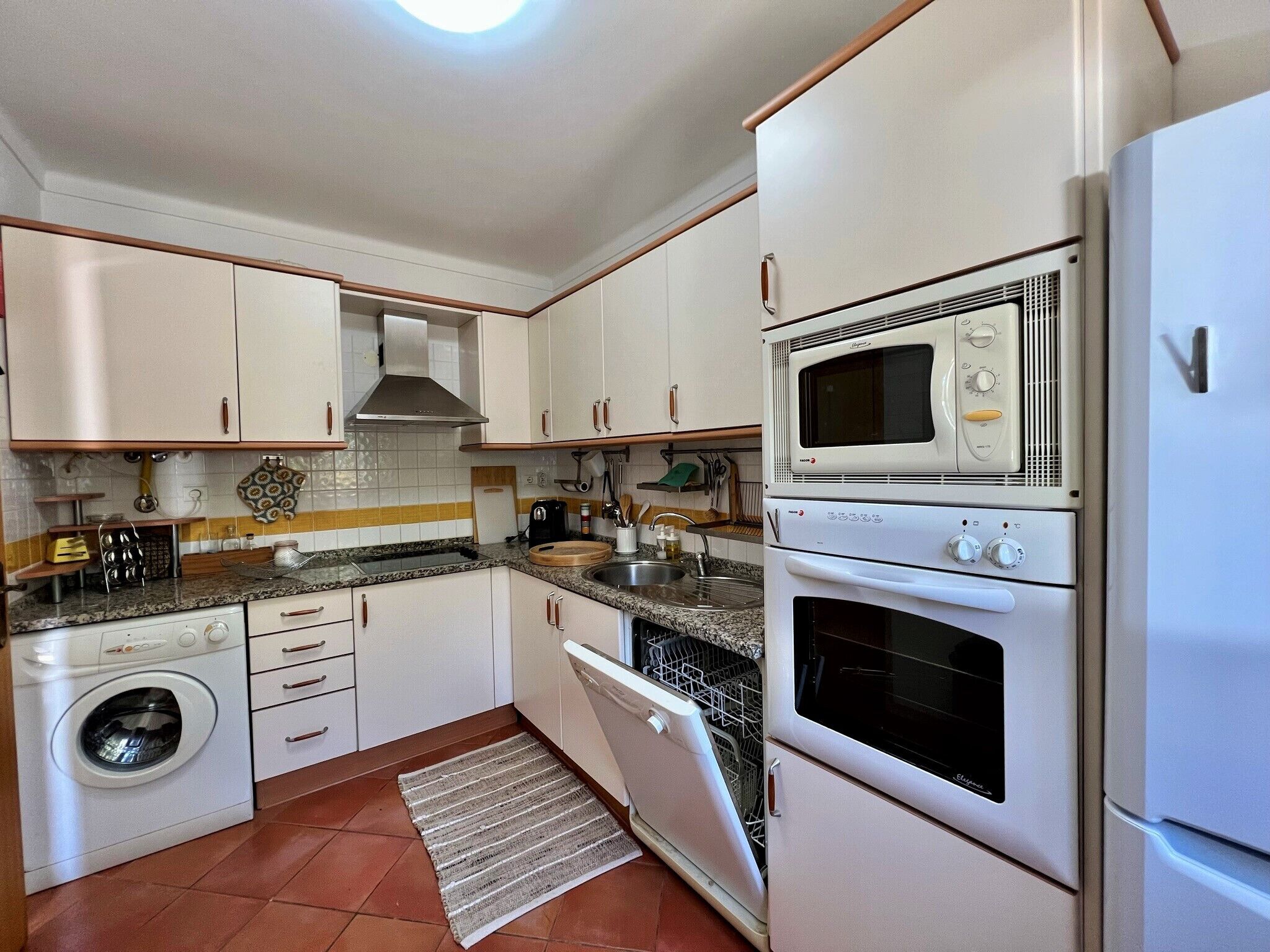 A compact kitchen with white cabinets, a built-in oven, microwave, and a washing machine.