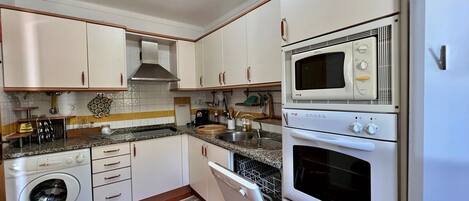 A compact kitchen with white cabinets, a built-in oven, microwave, and a washing machine.